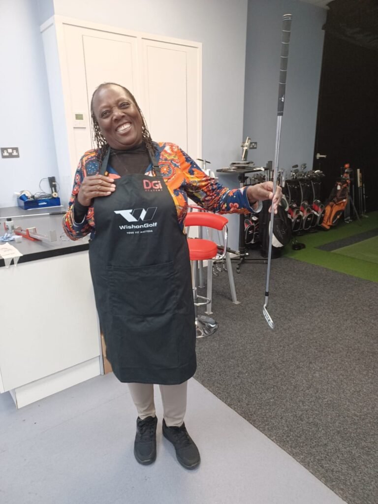 Woman wearing a "Wishon Golf" apron smiling and holding a golf club.